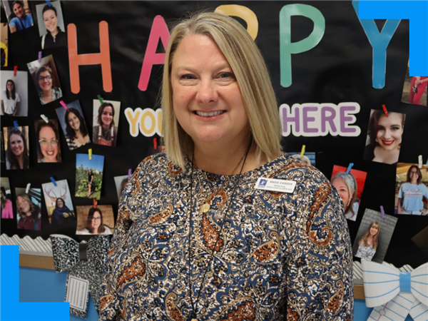  Angie Carder stands in front of a bulletin board with photos of other staff smiling.